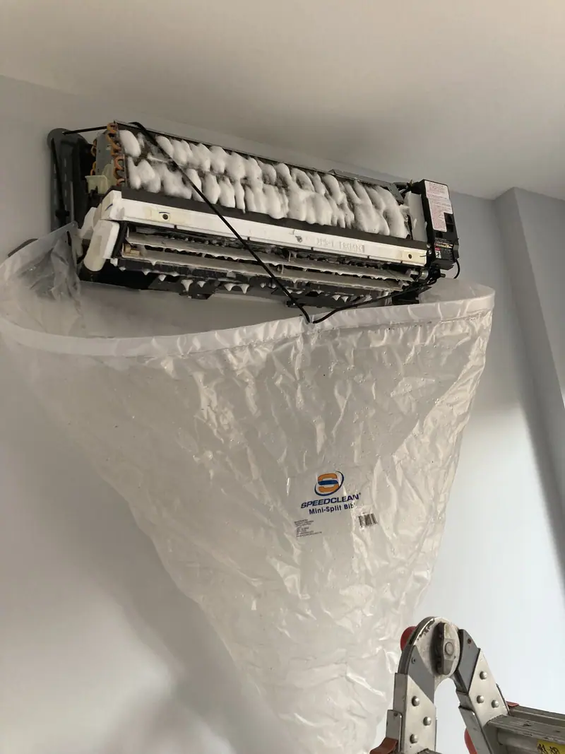 Mini split coil mid-cleaning with foam coil cleaner and a SpeedClean bib catching the runoff