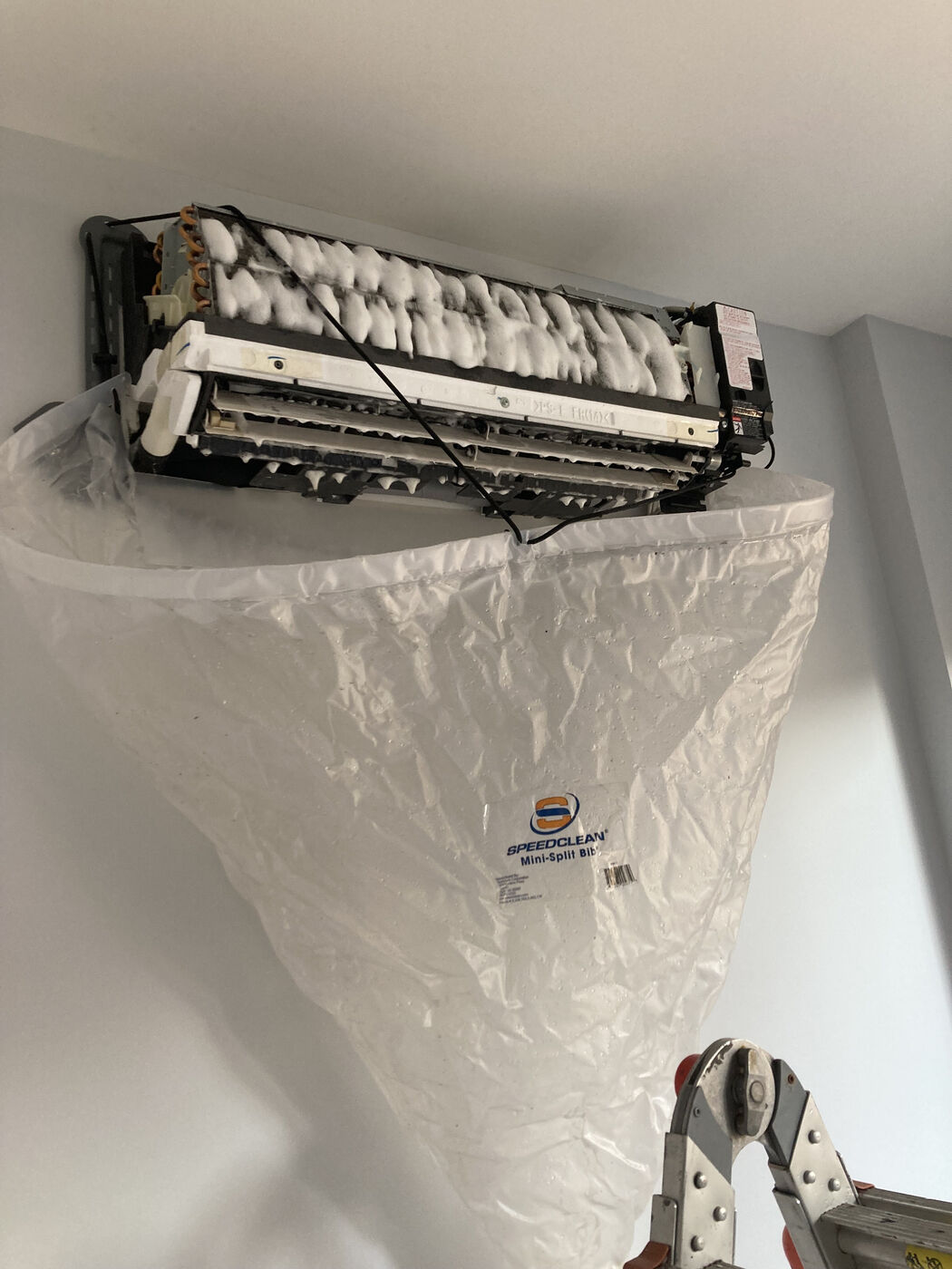 Mini split coil mid-cleaning with foam coil cleaner and SpeedClean bib catching runoff — Brooklyn ductless service
