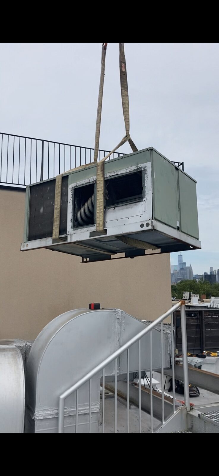 Crane removing an old rooftop AC unit with the Manhattan skyline behind