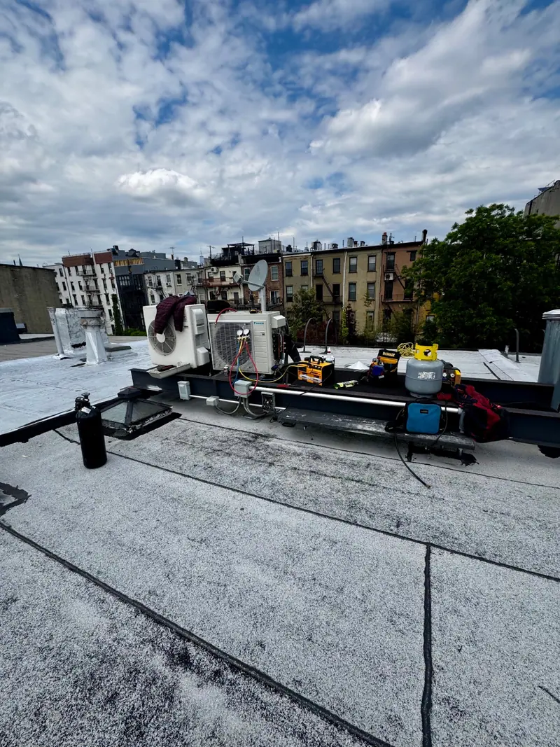 Daikin mini-split condenser on a rooftop rail being commissioned, with gauges, vacuum pump and nitrogen tank on site