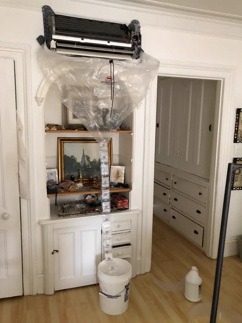 SpeedClean bib rigged under an opened mini-split wall head in a prewar apartment, draining to a bucket