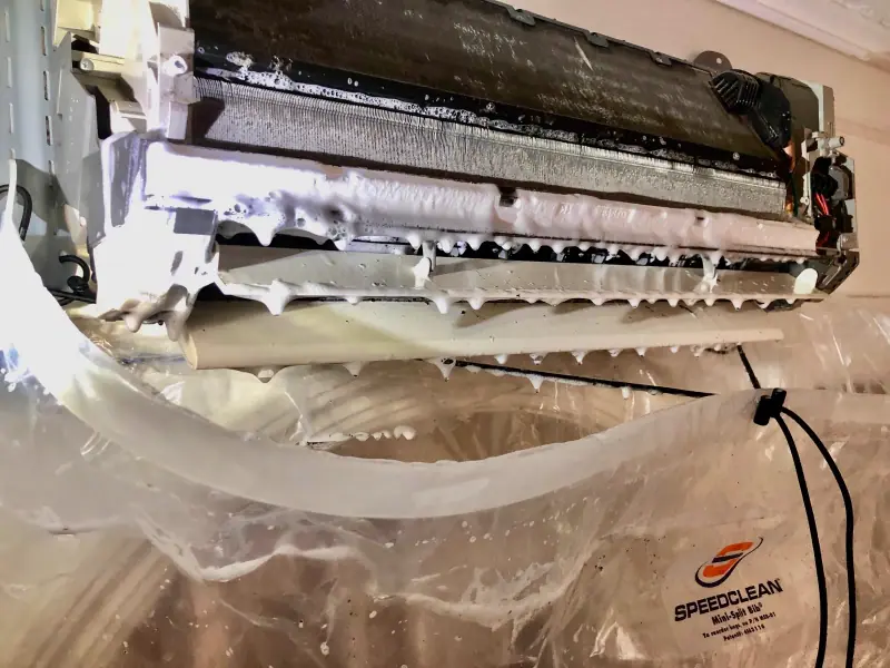 Foam coil cleaner working on an opened mini-split evaporator coil with a SpeedClean bib catching the runoff