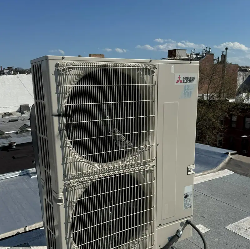 Mitsubishi Electric Hyper-Heat outdoor unit on a Brooklyn rooftop with rowhouses behind