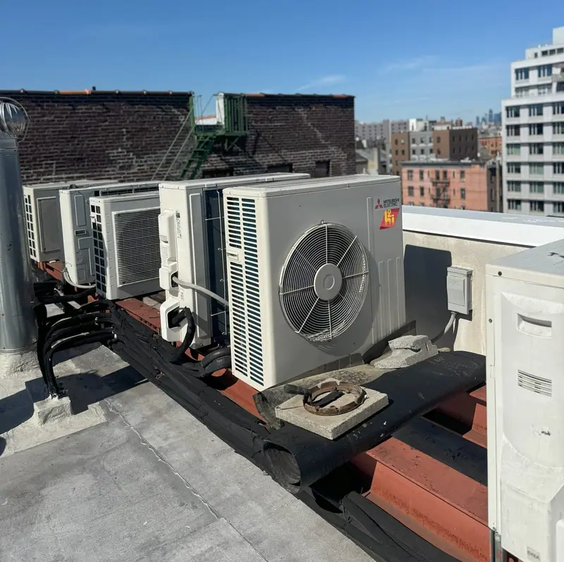 Mitsubishi Electric condenser at the front of a rooftop rail of ductless units, with line sets, on a Brooklyn roof