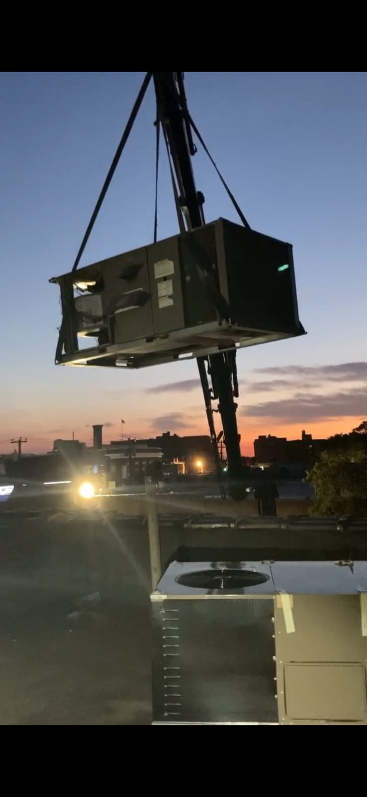 Brownstone Heating crane lifting a rooftop HVAC unit at sunset in Brooklyn