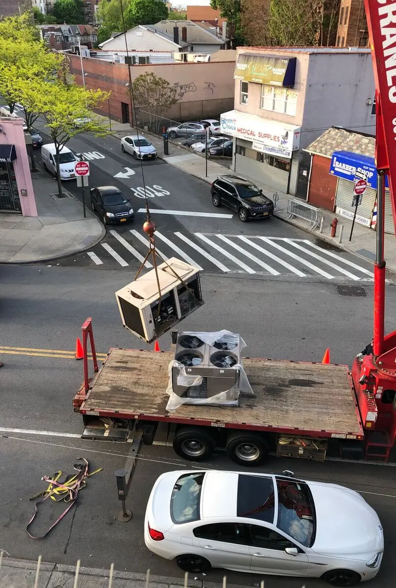 Crane lifting a rooftop AC unit over a Brooklyn street during a real Brownstone Heating & Air Conditioning install